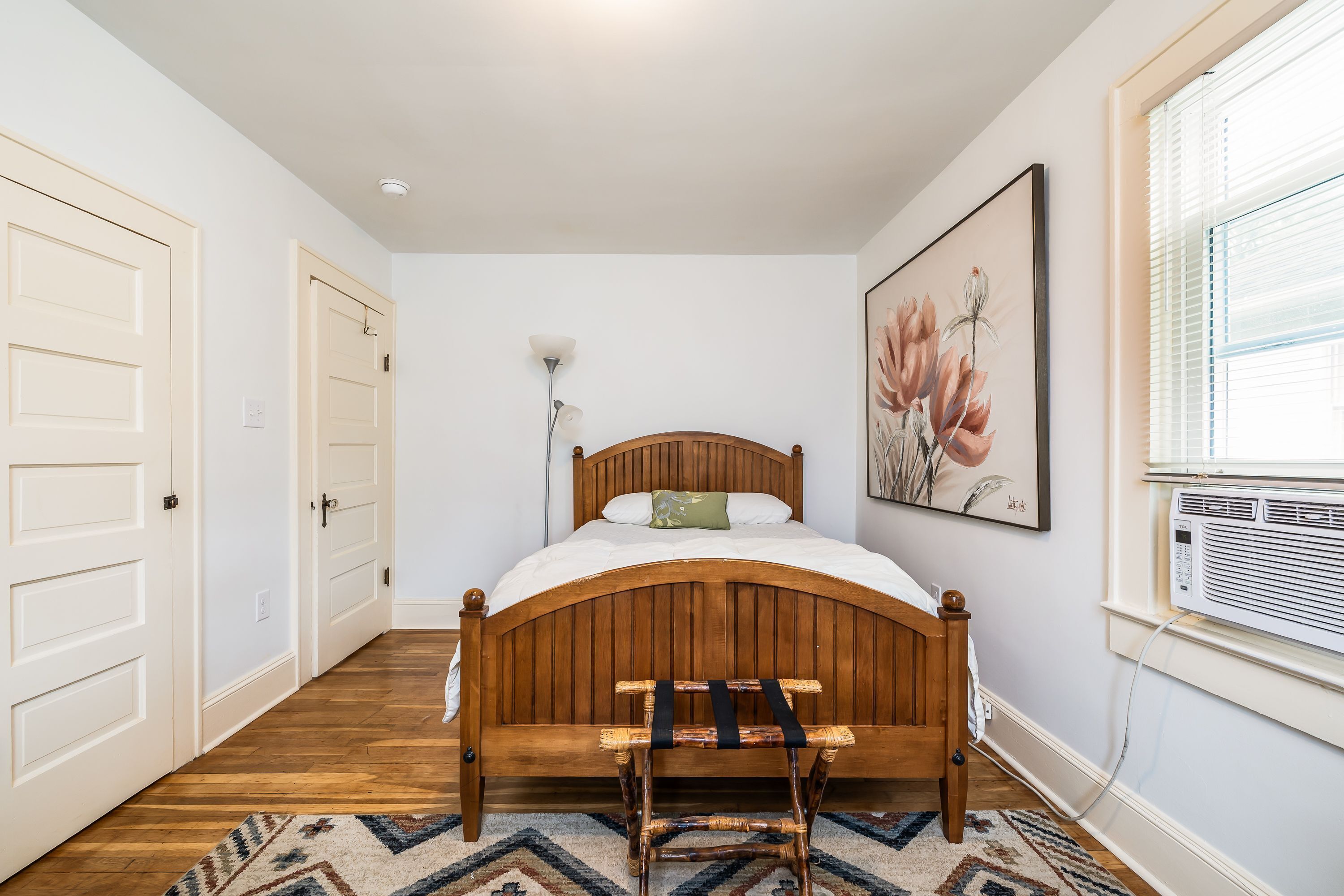 A bedroom with a wooden bed, a chair, a painting, and a window with blinds.