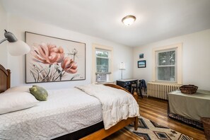 Une chambre à coucher avec un lit, un bureau, un radiateur et une fenêtre avec des stores.