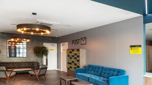 A modern reception area with a blue sofa, a wooden bench, and a post office sign. - Student Only Anglia House (Cambridge)