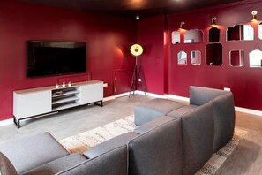 A modern living room with a large flat-screen TV, a grey sofa, a white entertainment unit, and a floor lamp. - Student Only Anglia House (Cambridge)
