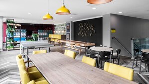 A modern dining area with a long wooden table, yellow chairs, and pendant lighting. - Student Only Anglia House (Cambridge)