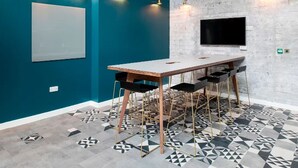 A conference room with a long table and chairs, a mounted TV, and patterned flooring. - Student Only Anglia House (Cambridge)
