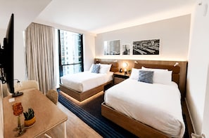 Una habitación de hotel con dos camas, un escritorio, un televisor y ventanas amplias.