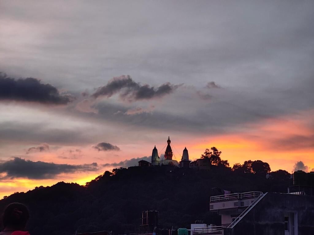 A view of a hilltop with a building featuring multiple domes, surrounded by trees and a cloudy sky.