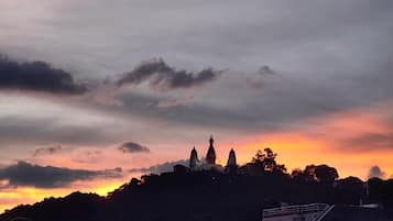 A view of a hilltop with a building featuring multiple domes, surrounded by trees and a cloudy sky.