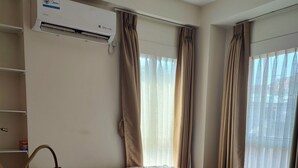 Et hotelværelse med to senge, en fastgjort aircondition og et vindue med gardiner.