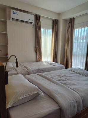 Habitación de hotel con dos camas, aire acondicionado instalado en la pared y una ventana con cortinas.