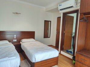 Habitación de hotel con dos camas, un armario, un espejo y un equipo de aire acondicionado.