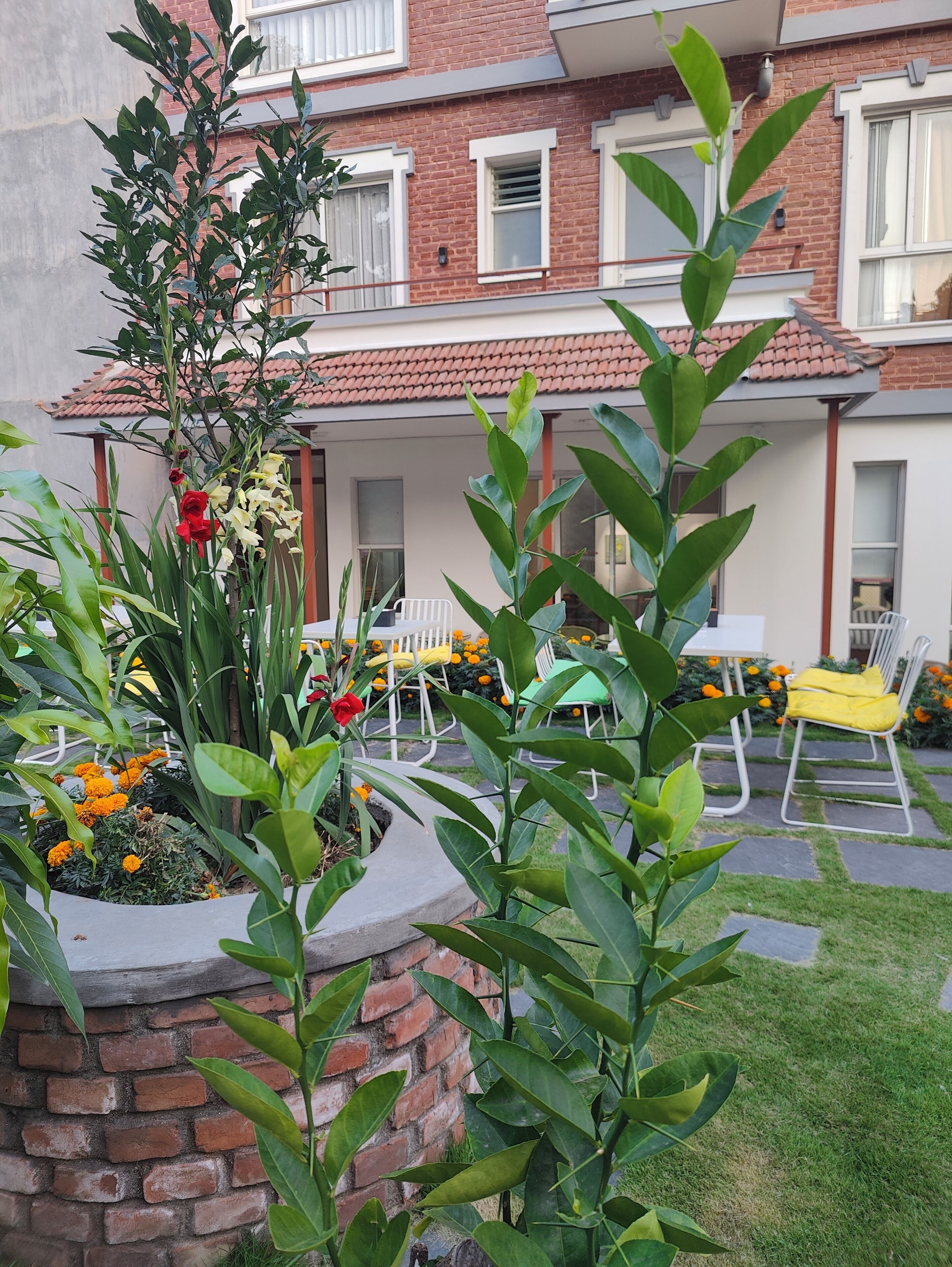 A brick building with a patio area, outdoor seating, and a garden with plants and flowers.