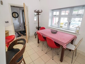 Ein Essbereich mit rot-weiß gestreiftem Tisch und roten Stühlen, sowie einem Fenster mit Rollläden.
