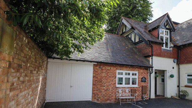 A brick house with a white garage door, a small window, and a metal bench outside. - Tudor Lodge (Birmingham)