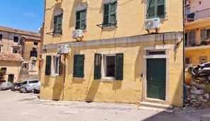A yellow building with green shutters, air conditioning units, and a stone wall. - Casa Dei Padri #2 - Historic Center (Corfu)