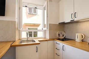 A compact kitchen with a window, a sink, a stove, and cabinets. - Casa Dei Padri #2 - Historic Center (Corfu)