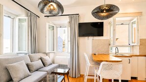A modern living space with a sofa, a coffee table, a TV, and a kitchen area with a sink and stools. - Casa Dei Padri #2 - Historic Center (Corfu)