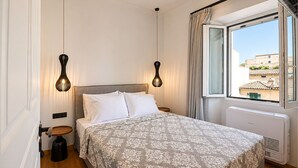 A bedroom with a bed, two pendant lights, a radiator, and a window with curtains. - Casa Dei Padri #2 - Historic Center (Corfu)
