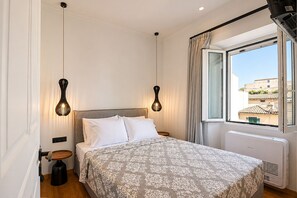 A bedroom with a bed, two pendant lights, a radiator, and a window with curtains. - Casa Dei Padri #2 - Historic Center (Corfu)