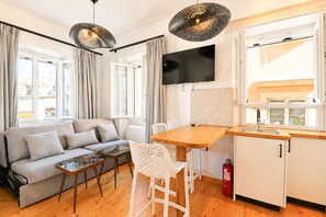 A modern living space with a sofa, a dining table, chairs, a TV, and a kitchen area. - Casa Dei Padri #2 - Historic Center (Corfu)