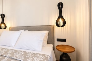 A neatly made bed with white linens and a patterned throw, a round wooden nightstand, and two wall-mounted lamps with a unique design. - Casa Dei Padri #2 - Historic Center (Corfu)