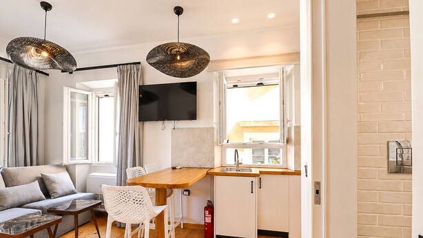 A modern kitchen with a wooden countertop, white cabinets, a built-in TV, and a window with curtains. - Casa Dei Padri #2 - Historic Center (Corfu)