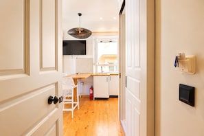A hallway leading to a kitchen with white cabinetry, a wooden countertop, and a hanging pendant light. - Casa Dei Padri #2 - Historic Center (Corfu)