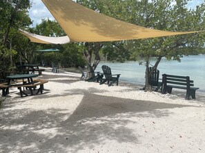 A beachside picnic area with tables and chairs, a shaded canopy, and a view of the water. - Come RELAX in this cozy 2-bedroom house in beautiful Key Largo (Key Largo)
