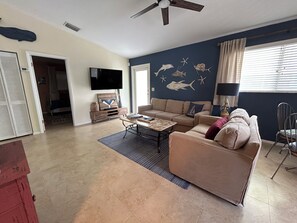 A living room with a beige sofa, a coffee table, a flat-screen TV mounted on the wall, and a ceiling fan. - Come RELAX in this cozy 2-bedroom house in beautiful Key Largo (Key Largo)