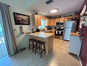 A kitchen with wooden cabinets, a central island with stools, a microwave, an oven, and a refrigerator. - Come RELAX in this cozy 2-bedroom house in beautiful Key Largo (Key Largo)