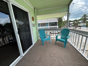 A covered outdoor area with a sliding glass door, two chairs, a small table, and a view of a building with a white fence. - Come RELAX in this cozy 2-bedroom house in beautiful Key Largo (Key Largo)
