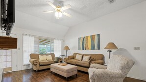 A living room with a ceiling fan, two sofas, a patterned armchair, and a painting on the wall.