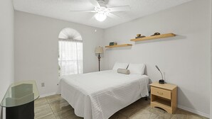 A bedroom with a bed, a nightstand, a lamp, a ceiling fan, and a window with curtains.