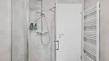 A modern bathroom with a glass shower enclosure, a white door, and a white towel rack.