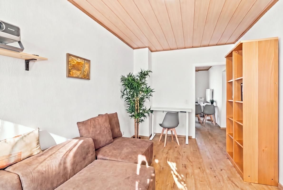 Un salon moderne avec un canapé marron, une petite table, une plante en pot et un plafond en bois.