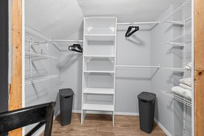 A closet with white shelving, a black chair, and two trash bins.