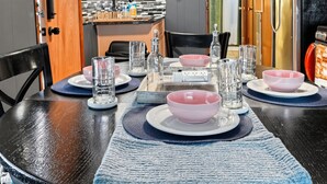 Un coin repas avec une table dressée pour quatre personnes, une cuisine en arrière-plan et une porte donnant sur une autre pièce.