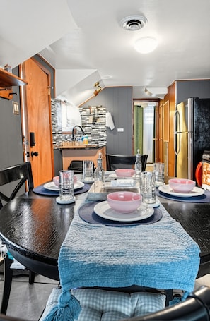 A dining area with a table set for four, a kitchen in the background, and a door leading to another room.