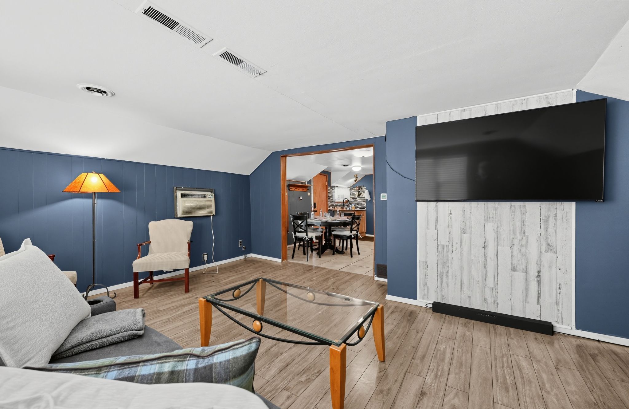 A modern living room with a sofa, a glass coffee table, a lamp, and a TV mounted on the wall.