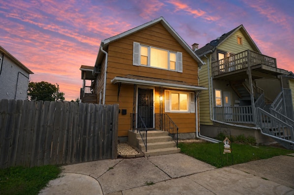 A two-story house with a front porch, a wooden fence, and a small garden.