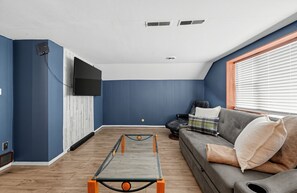 A living room with a ping pong table, a sofa, and a TV mounted on the wall.