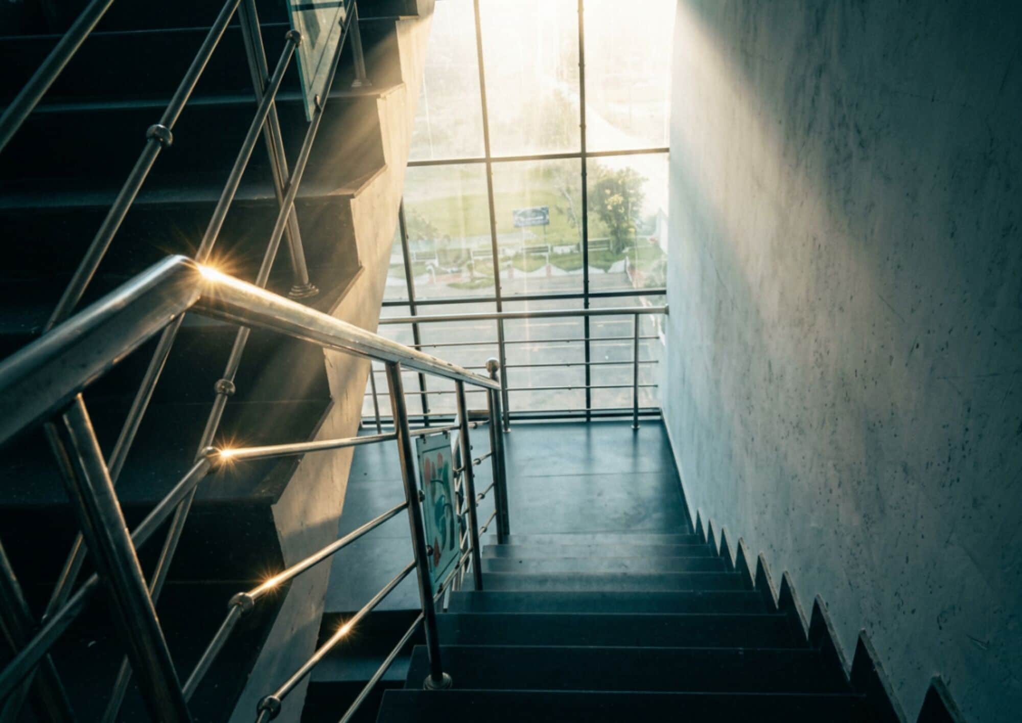 Eine Treppe mit Metallgeländern führt zu einer höheren Etage, umgeben von Wänden und einem Fenster.