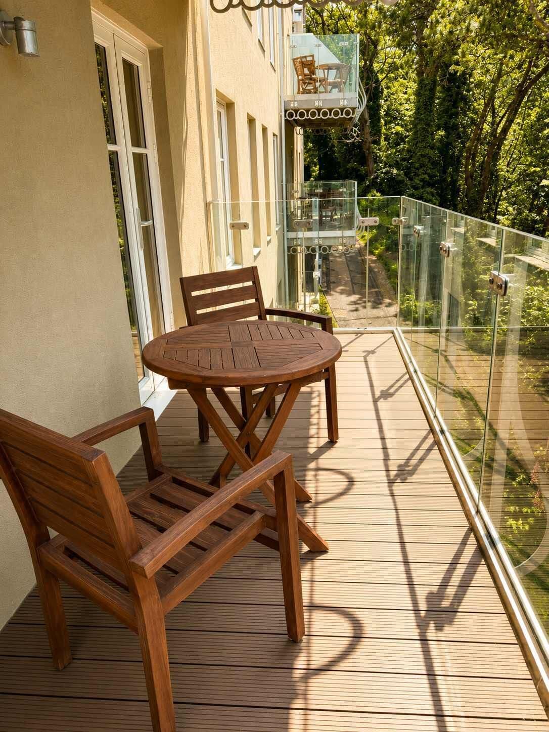 Une terrasse en bois avec une balustrade en verre, une table ronde et deux chaises.
