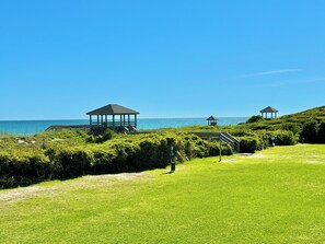 A coastal area with three gazebos, a grassy path, and a view of the ocean.