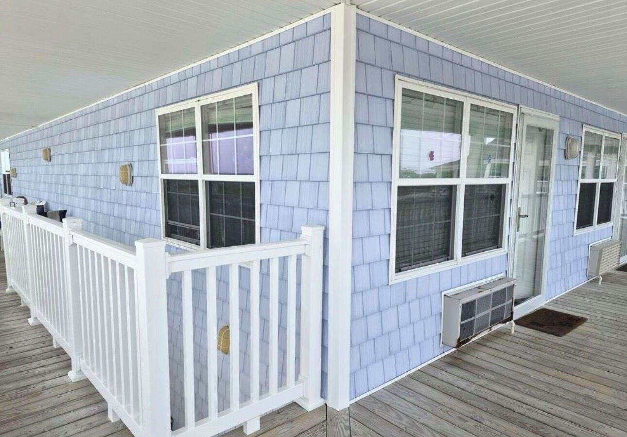 A covered outdoor area with a white railing, light blue siding, and a wooden deck.