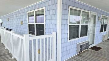A covered outdoor area with a white railing, light blue siding, and a wooden deck.