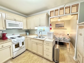 A compact kitchen with a microwave, stove, sink, and a small trash bin.