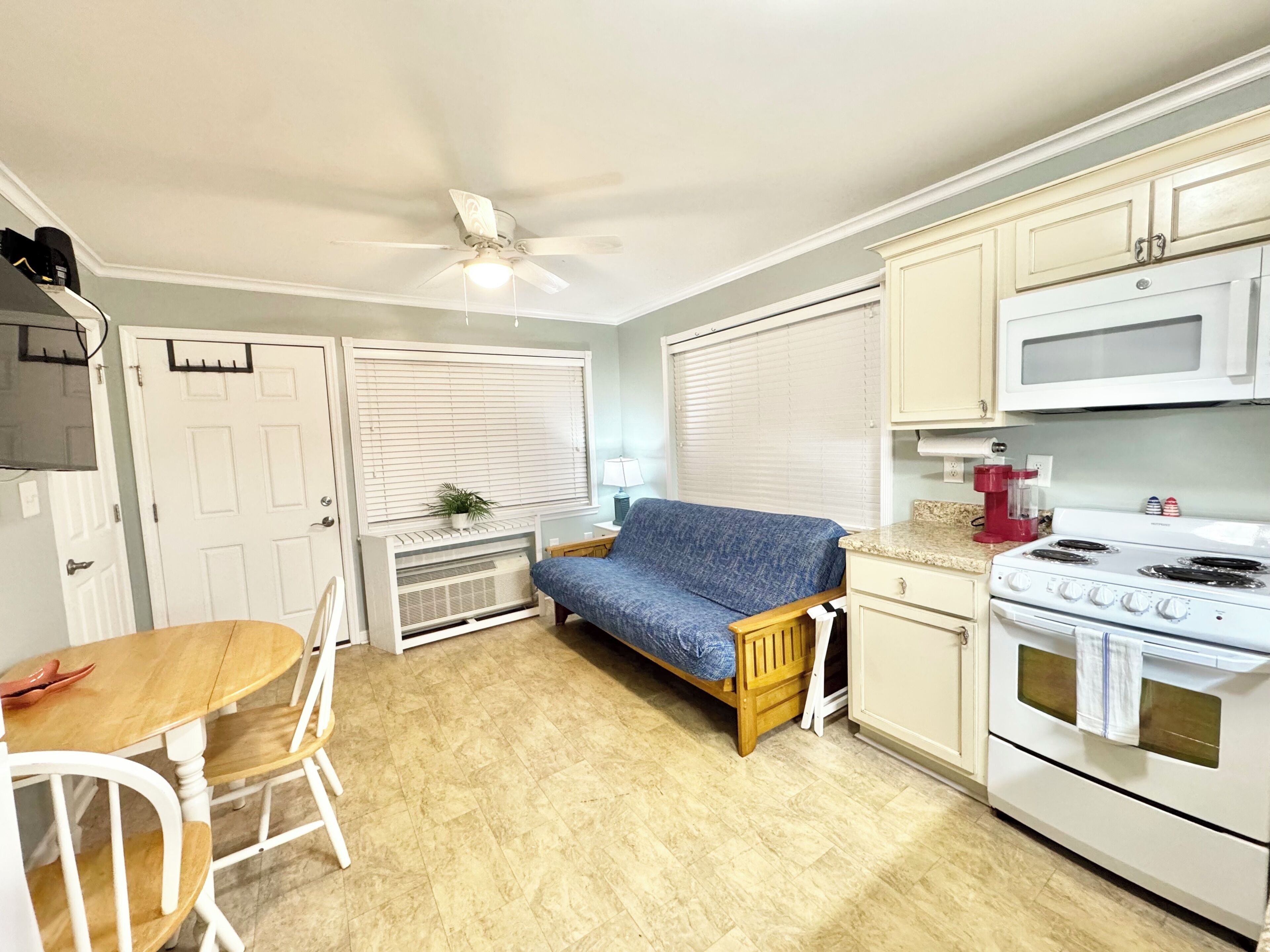 A compact kitchen with a dining area, a ceiling fan, a stove, and a couch.