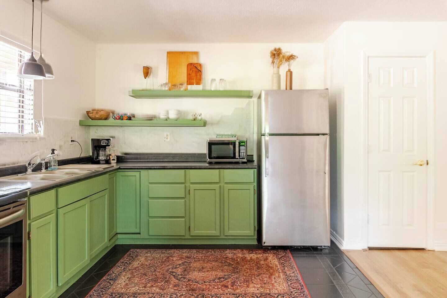 A kitchen with green cabinets, a stainless steel refrigerator, a microwave, and a coffee maker.