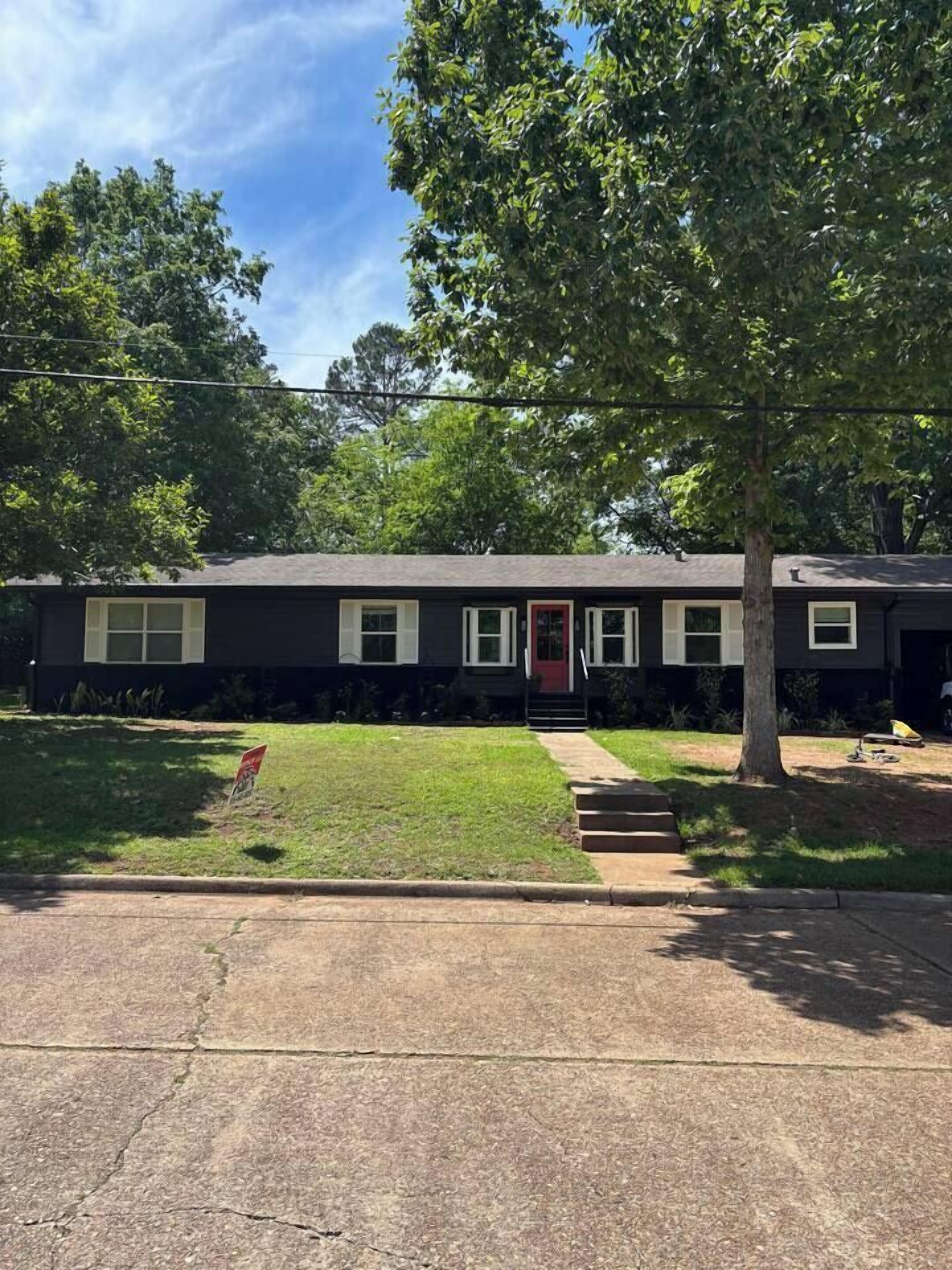 A single-story house with a front yard, a driveway, and a tree.