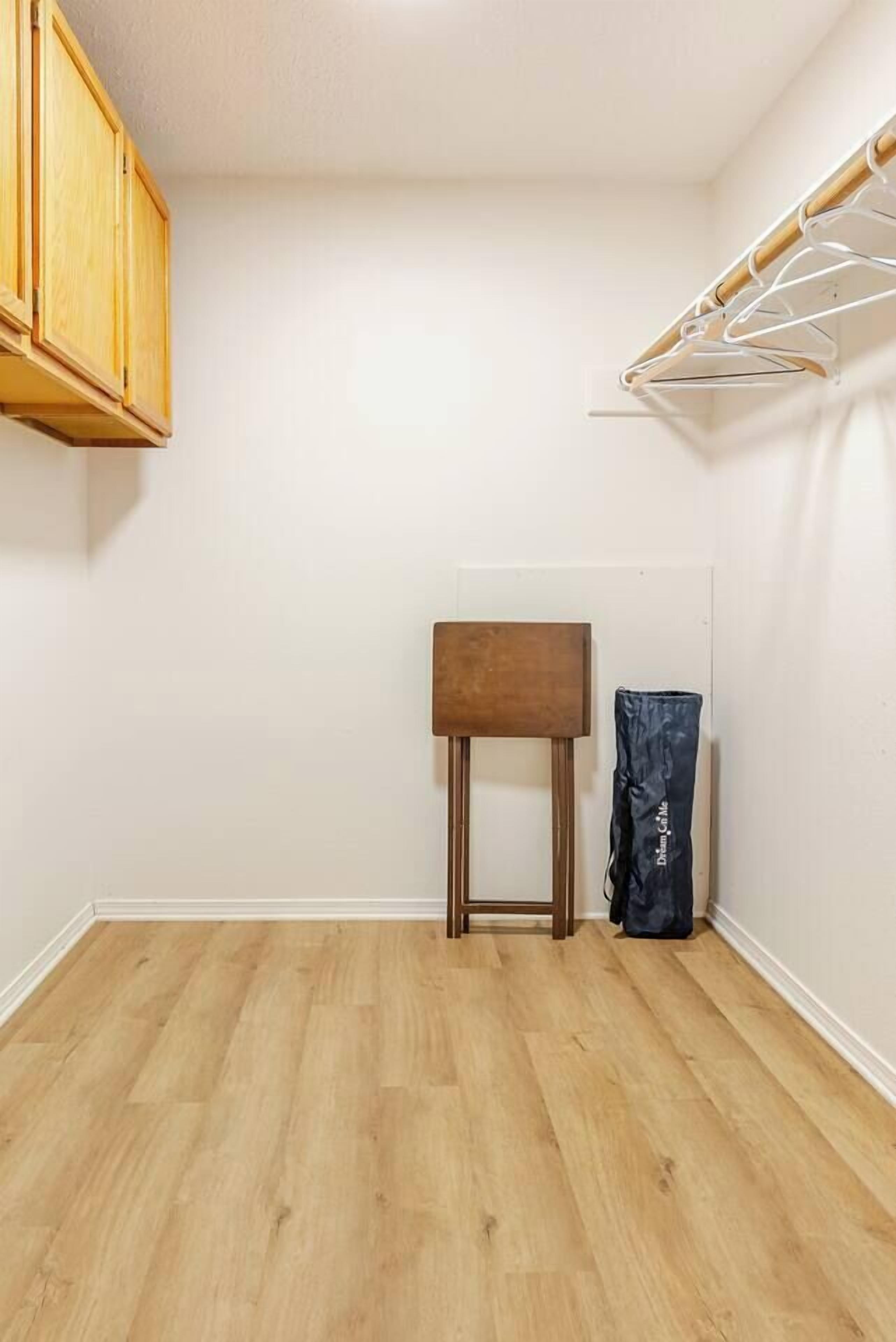 A room with a wooden cabinet, a small wooden stool, and a hanging clothes rack.