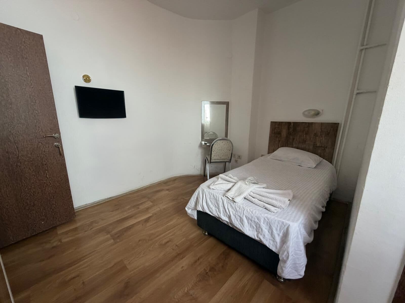 Un dormitorio con cama, espejo, televisor y suelo de madera.