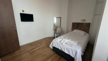 Un dormitorio con cama, espejo, televisor y suelo de madera.